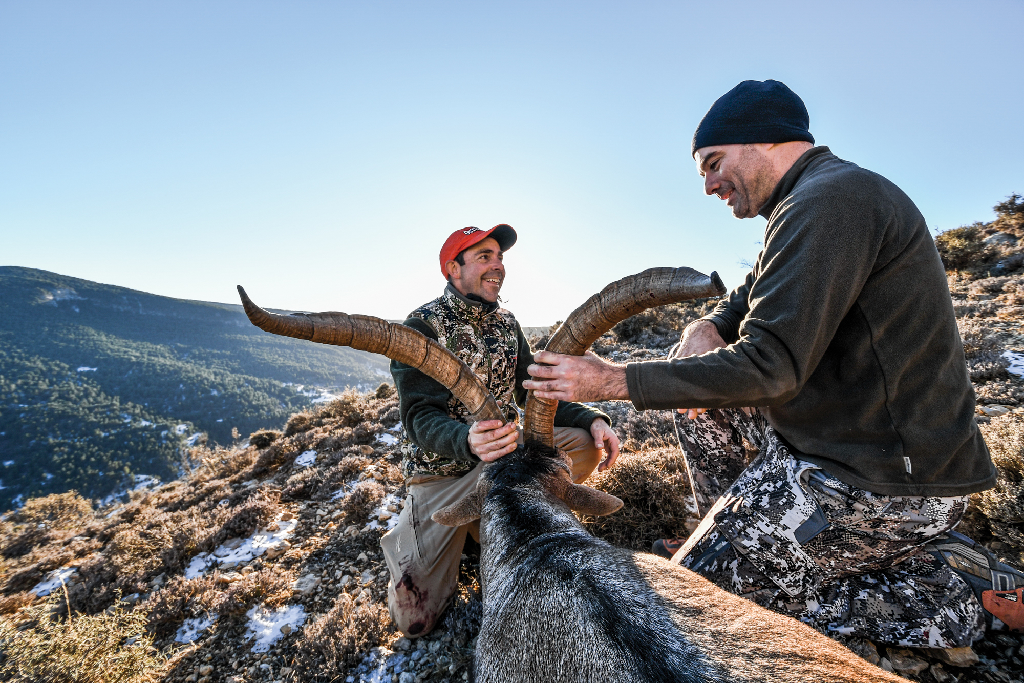 A hunter and his guide kneel beside a big Spanish ibex.