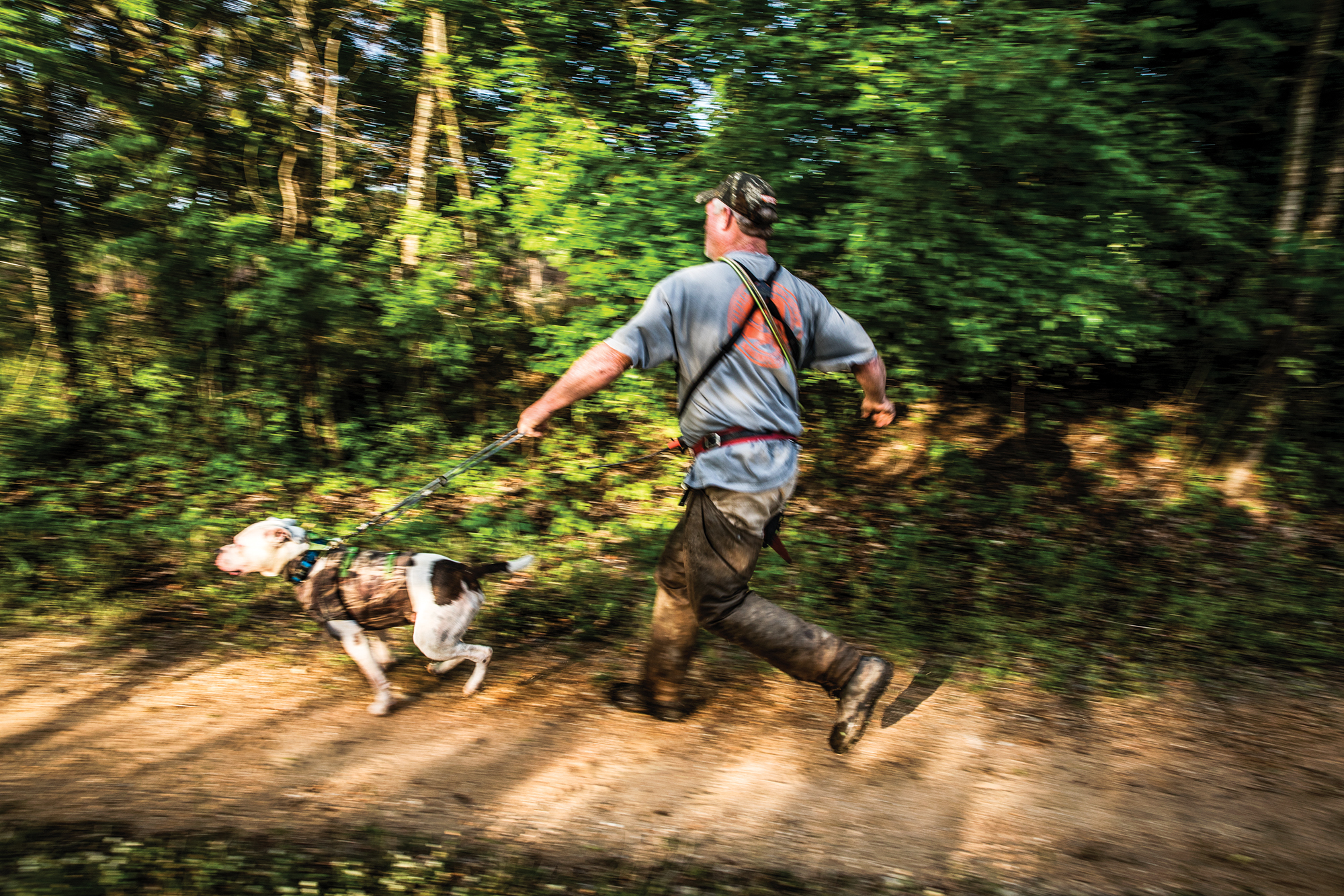 A hunter sprints to a bayed hog with his dog on a leash.