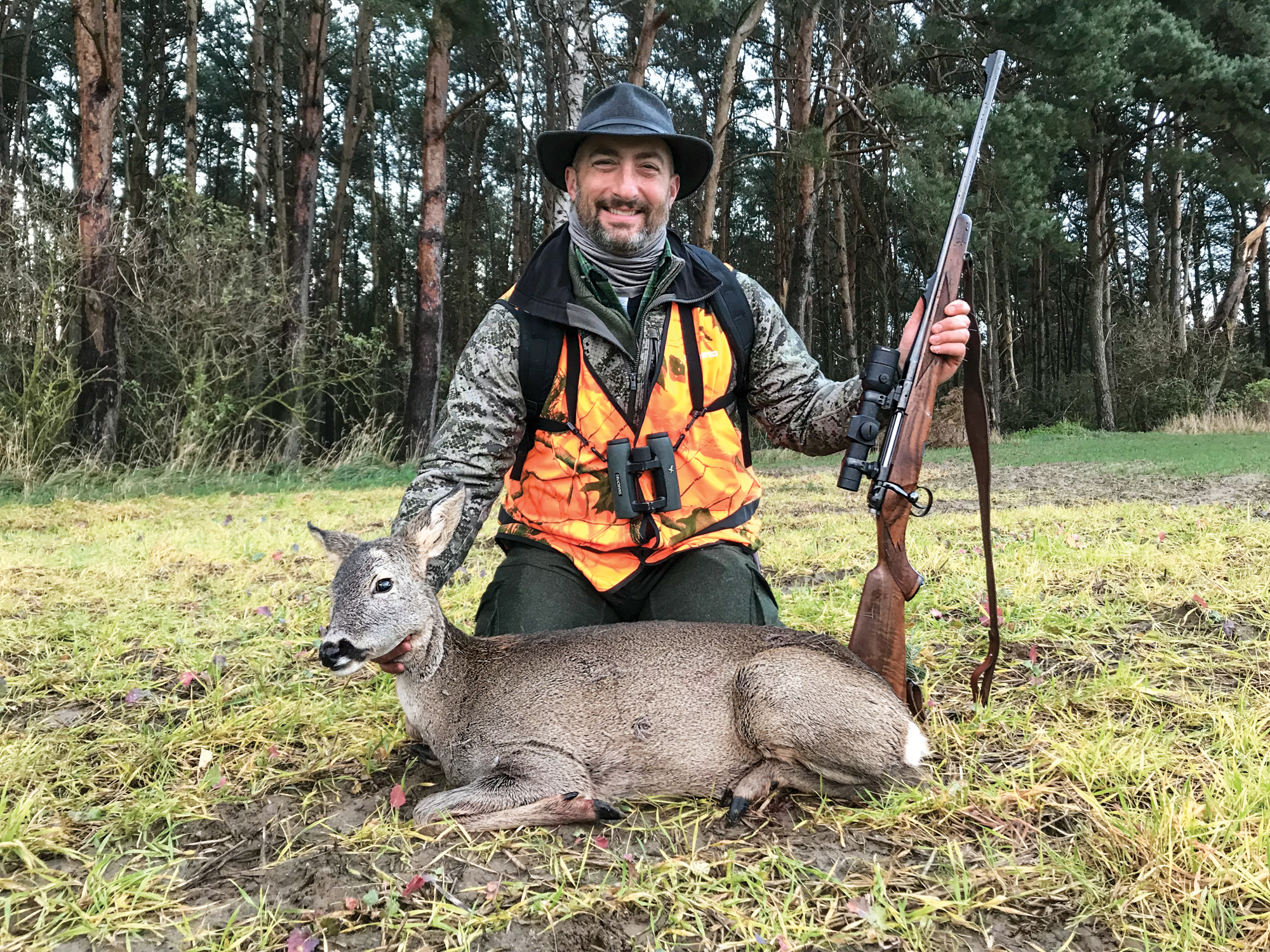 A hunter with an orange vest and a roe deer hind.