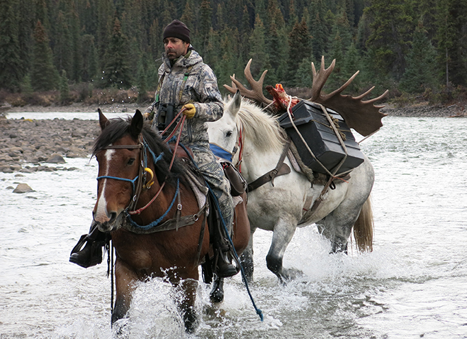<em>The author leads a loaded pack horse across British Columbia's swift Spatsizi River.</em>