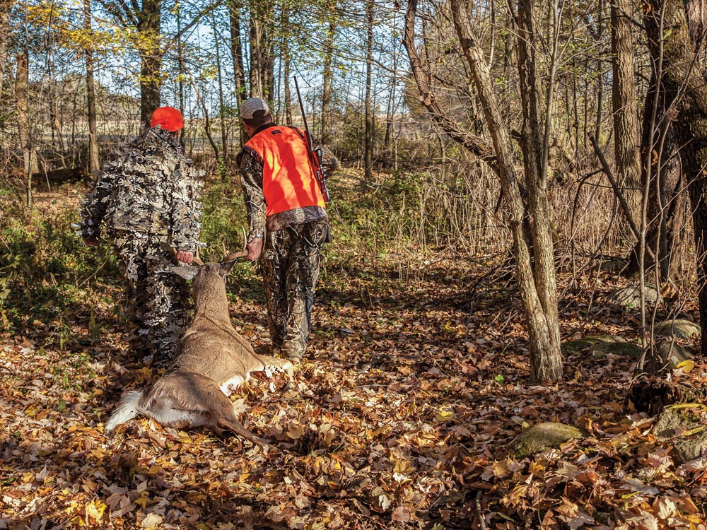 two hunters dragging a deer through forest