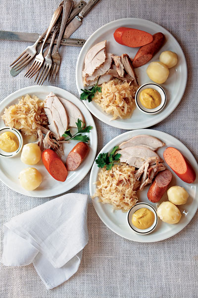 <strong>Turkey with Sauerkraut, Riesling, and Pork Sausages</strong> <strong>SERVES 10 - 12</strong> - Braised with wine, sauerkraut, apples, and onions, this turkey comes out incredibly moist and aromatic. <strong>12 juniper berries</strong> <strong>6 cloves garlic, smashed</strong> <strong>6  sprigs fresh parsley</strong> <strong>6 sprigs fresh thyme</strong> <strong>6 whole cloves</strong> <strong>3 bay leaves</strong> <strong>1 cup rendered duck fat</strong> <strong>3 onions, thinly sliced</strong> <strong>Kosher salt and freshly ground black pepper, to taste</strong> <strong>3 cups riesling</strong> <strong>1 lb. smoked slab bacon, cut into 3 ⁄4" strips</strong> <strong>4 lbs. raw sauerkraut, rinsed and drained</strong> <strong>2 Granny Smith apples, julienned</strong> <strong>1 10-12-lb. turkey</strong> <strong>12-14 strips thin-sliced bacon</strong> <strong>6 knackwurst</strong> <strong>6 bauernwurst</strong> <strong>16 small new potatoes, peeled</strong> <strong>Dijon mustard, for serving</strong> 1. Heat oven to 350°. Wrap juniper berries, garlic, parsley, thyme, cloves, and bay leaves in a piece of cheese-cloth; tie ends with twine; set aside. Heat duck fat in an 8-qt. pot over medium-high heat. Add onions, season with salt and pepper, cover, and cook, stirring occasionally, until soft, 18-20 minutes. Add wine and 1⁄2 cup water; boil for 2 minutes; transfer to a large roasting pan with spice bundle. 2. Arrange sliced slab bacon evenly over onions. Combine sauerkraut and apples in a bowl; transfer 3⁄4 of sauerkraut mixture over onion mixture. Season turkey with salt and pepper and stuff with remaining sauerkraut mixture. Drape thin-sliced bacon over top of turkey; secure with tooth-picks. Put turkey on top of sauerkraut in roasting pan. Cover with a sheet of parchment paper and 2 sheets of heavy-duty aluminum foil. Crimp foil tightly around edges of pan. Roast turkey until an instant-read thermometer inserted into deepest part of thigh reads 160°, about 3 hours. Transfer turkey to a cutting board; let rest for 20 minutes. Remove bacon and skin. 3. While turkey rests, bring a 5-qt. pot of salted water to a boil. Add sausages, reduce heat to medium-low, and simmer until tender, about 5 minutes. Transfer sausages to a large serving platter. Add potatoes to pot and simmer until tender, about 15 minutes. Transfer potatoes to platter. Carve turkey and arrange slices on platter. Serve with mustard. <strong>Pairing note:</strong> Dr. Konstantin Frank Semi Dry Riesling 2009 ($15), from New York's Finger Lakes, is an aromatic match for this fragrant dish. <em>This article was first published in <a href="http://www.saveur.com/article/Recipes/Turkey-with-Sauerkraut-Riesling-and-Pork-Sausages">Saveur</a> in Issue #133</em> <strong>Photo:</strong> Todd Coleman
