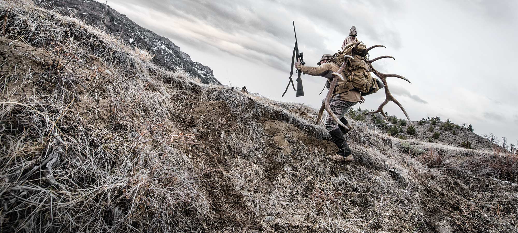 hunter carrying elk antlers up a hillside