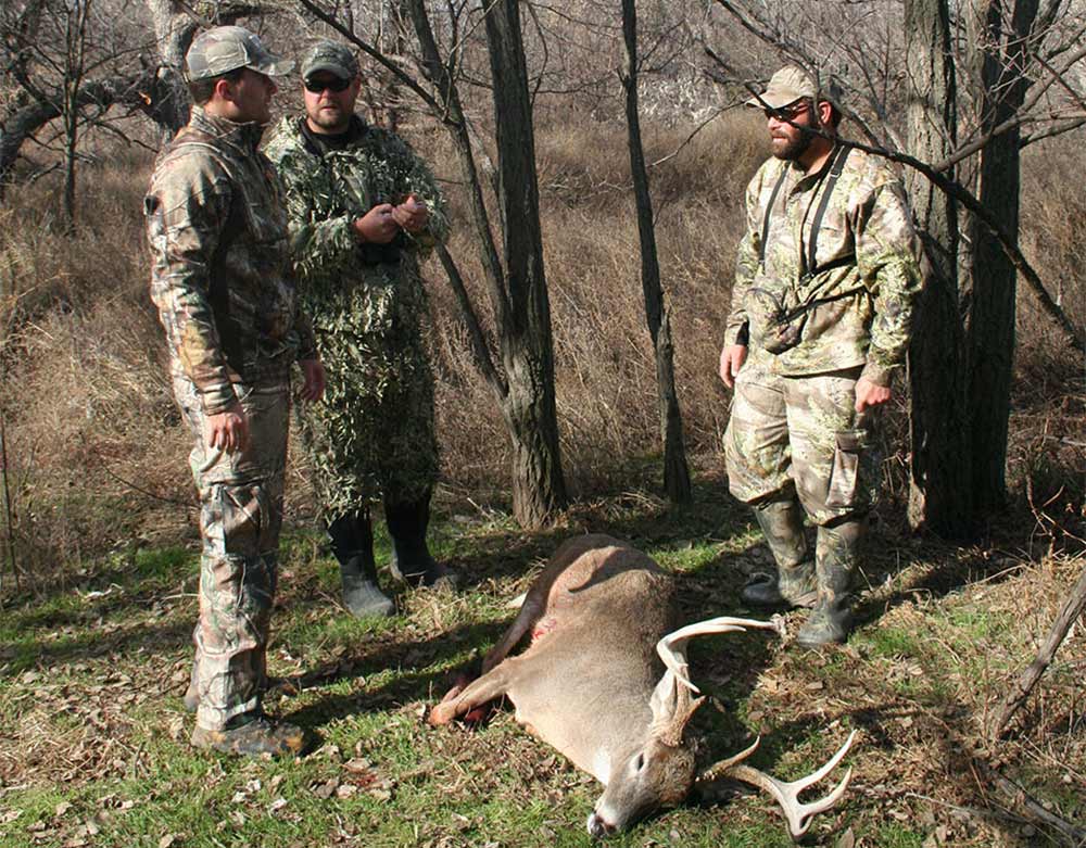 three hunters standing next to dead whitetail