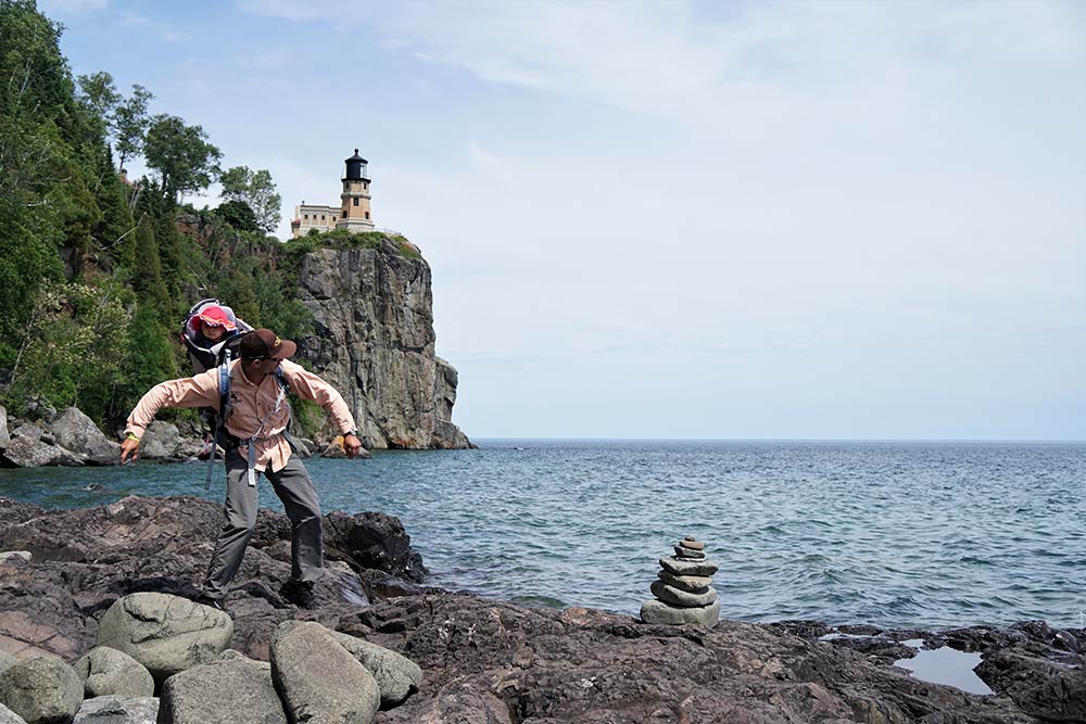 man skipping rocks at split rock lighthouse baby on his back