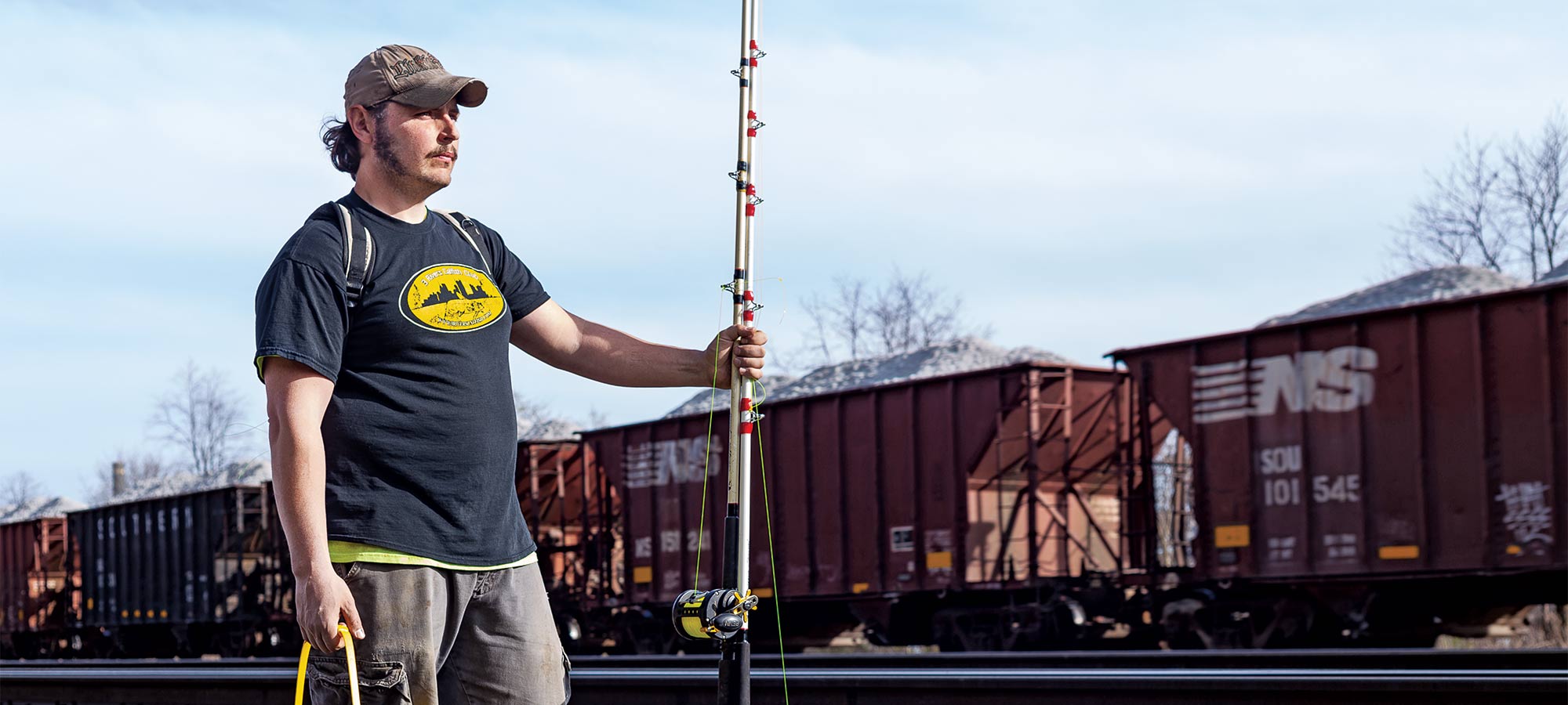 angler holding a fishing pole with a train in the background