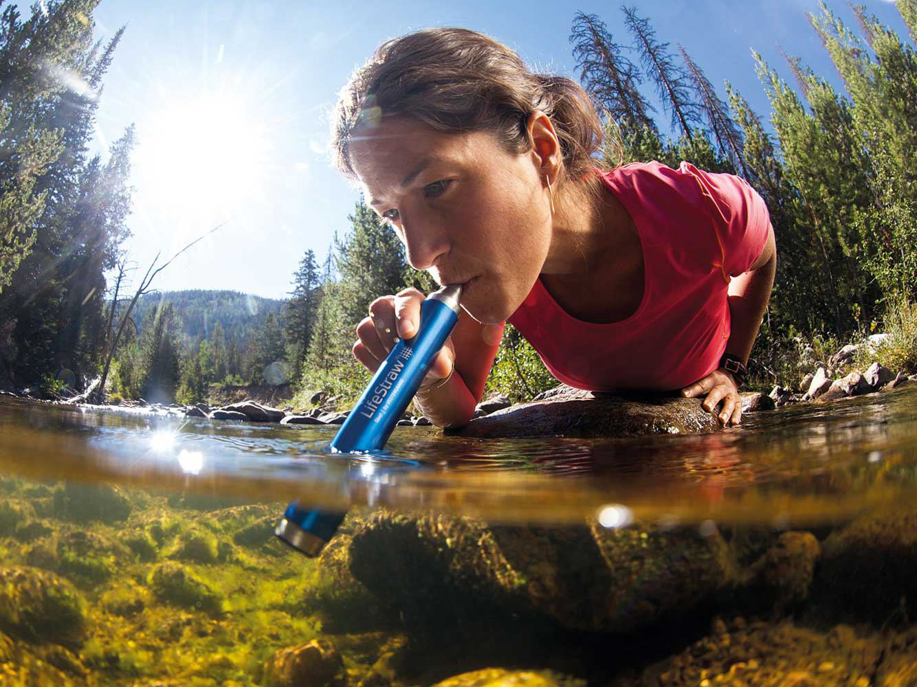 woman using lifestraw to drink water from river