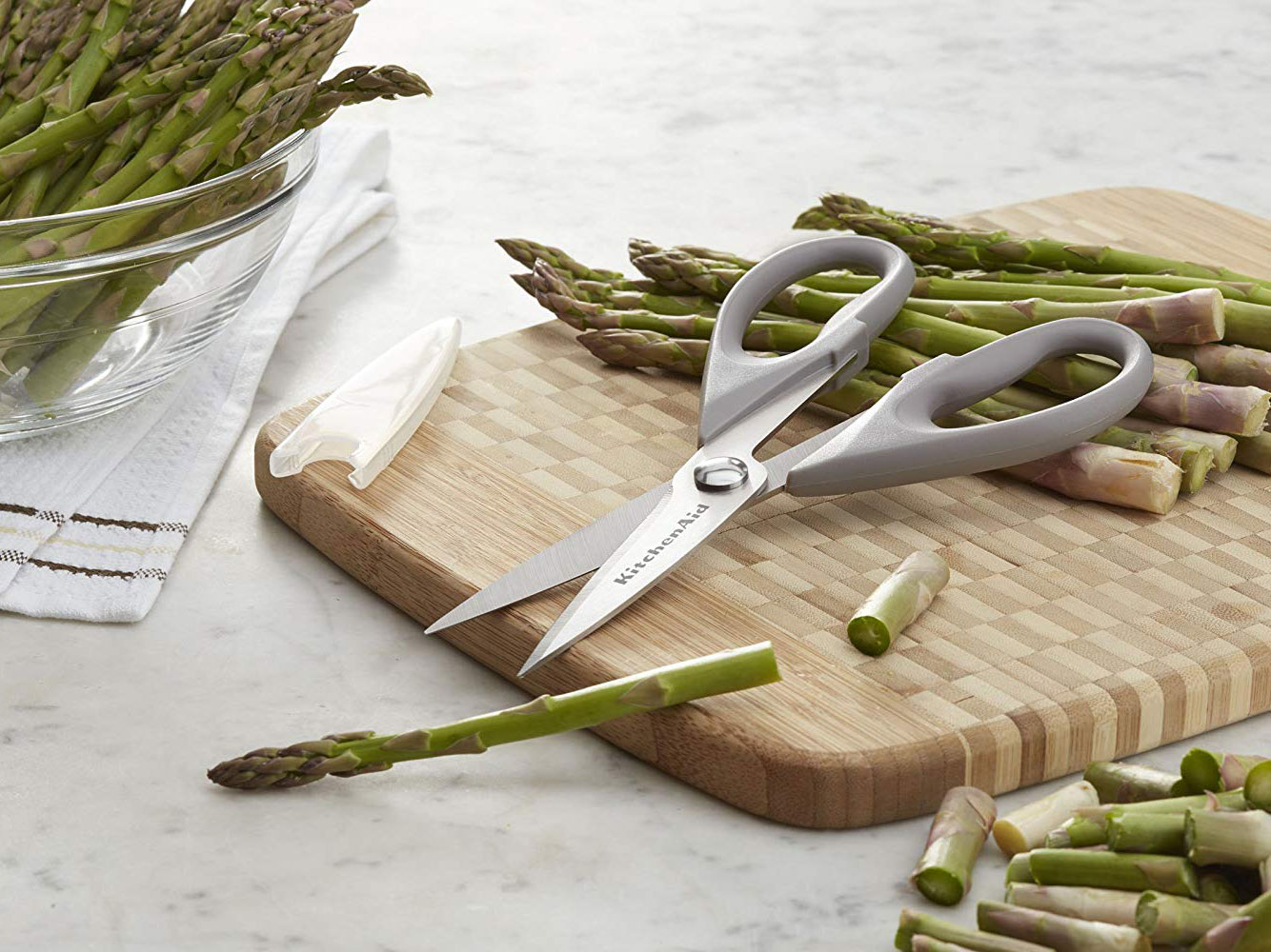 Kitchen shears on a cutting board beside asparagus
