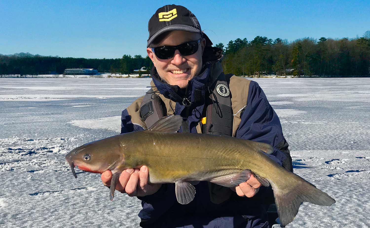 angler holding up a catfish caught in the ice.