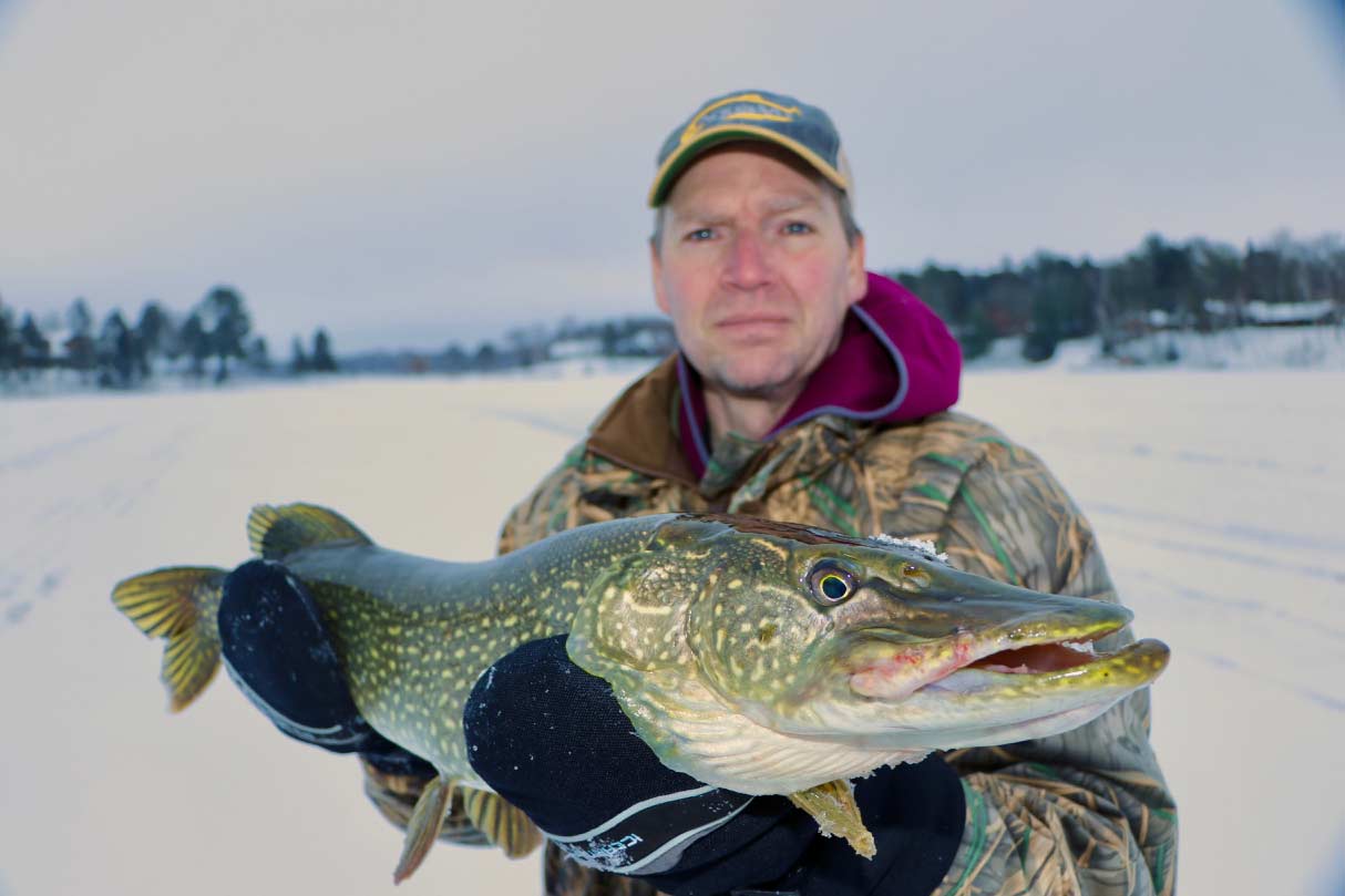 Angler holding up a pike caught while ice fishing.