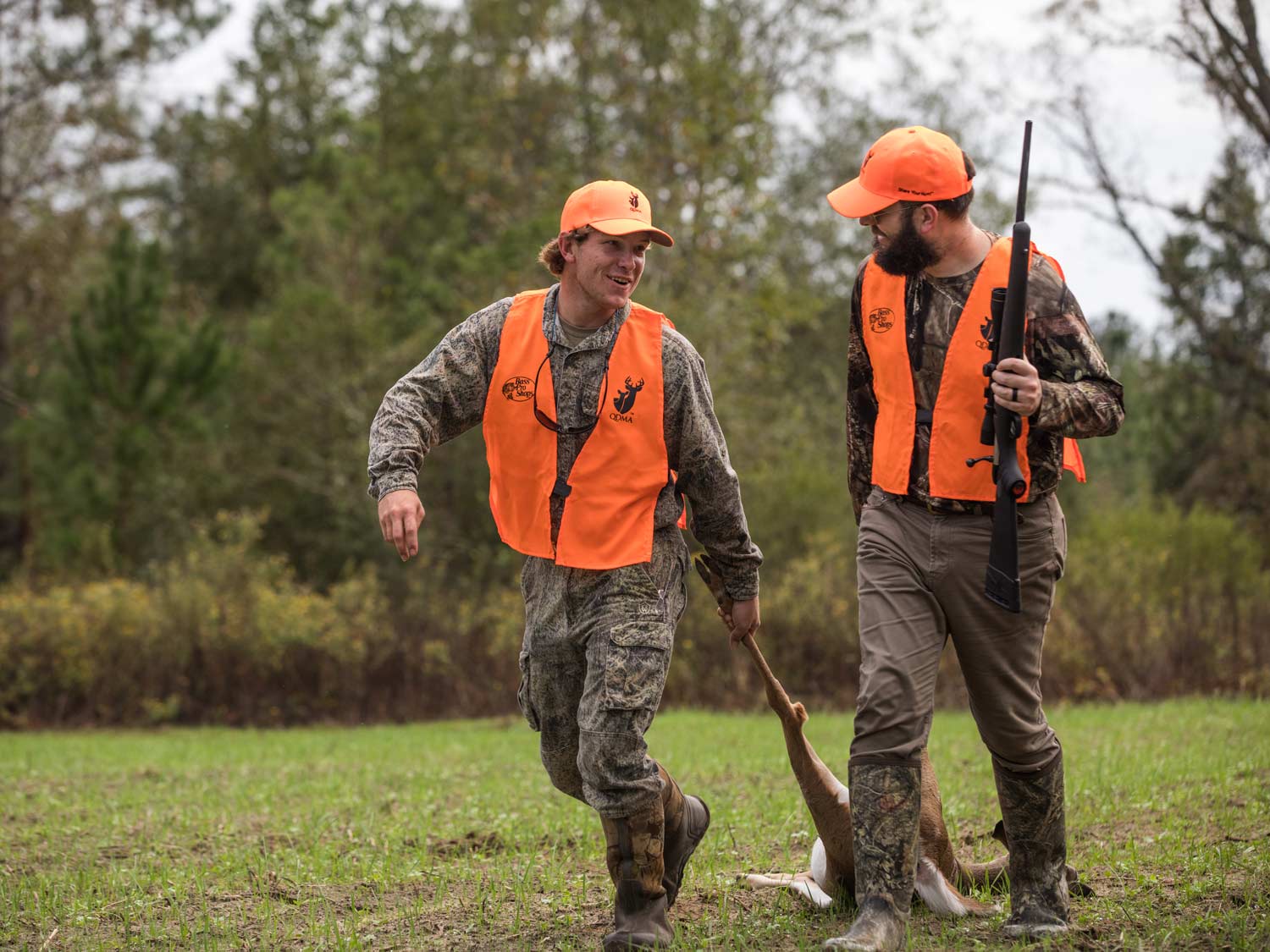 Two hunters in camo and orange vests drag a deer.