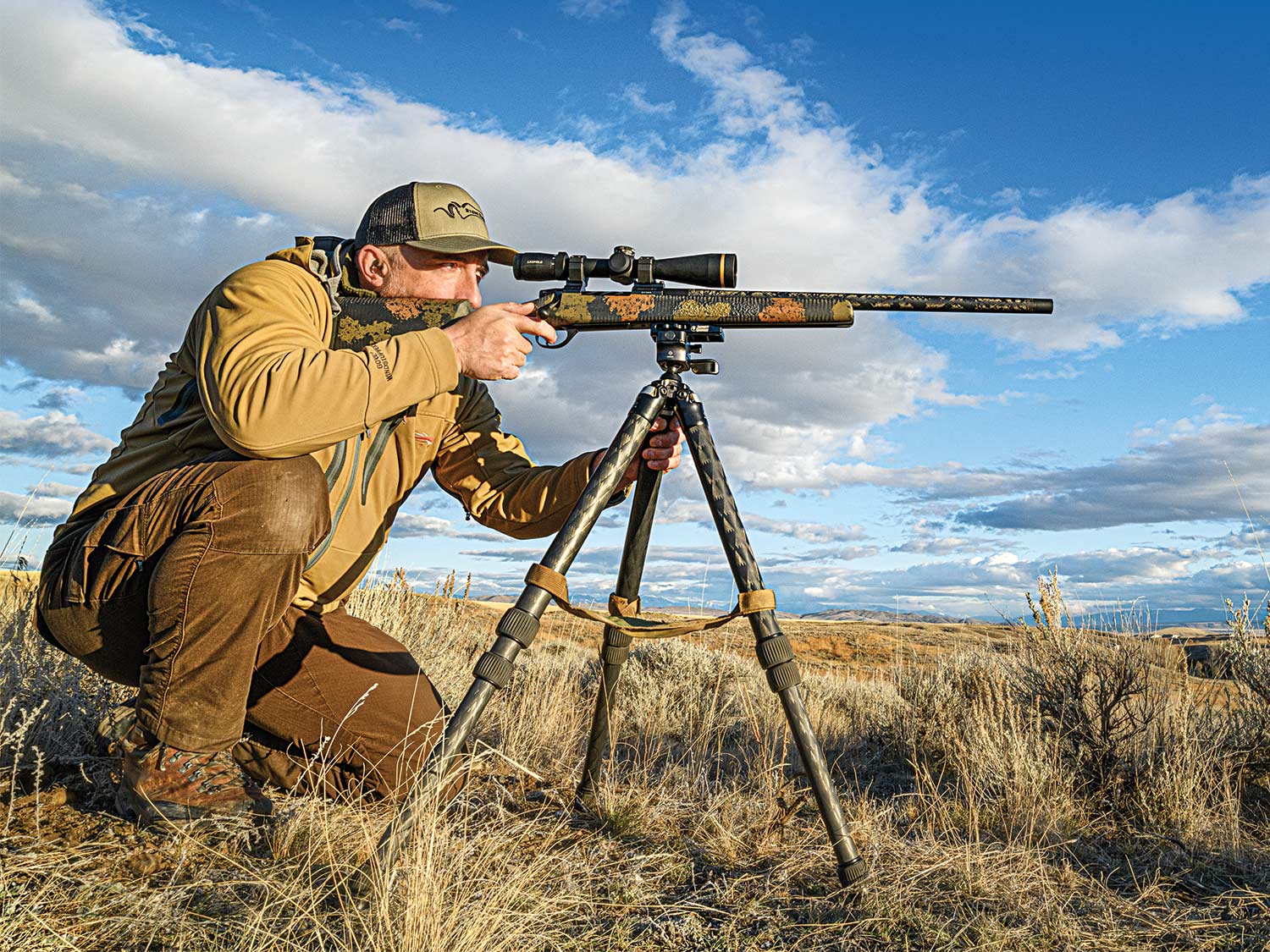 Hunter aiming a rifle in an open field.