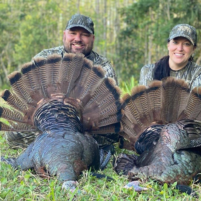 Two hunters kneeling behind Osceola turkeys.