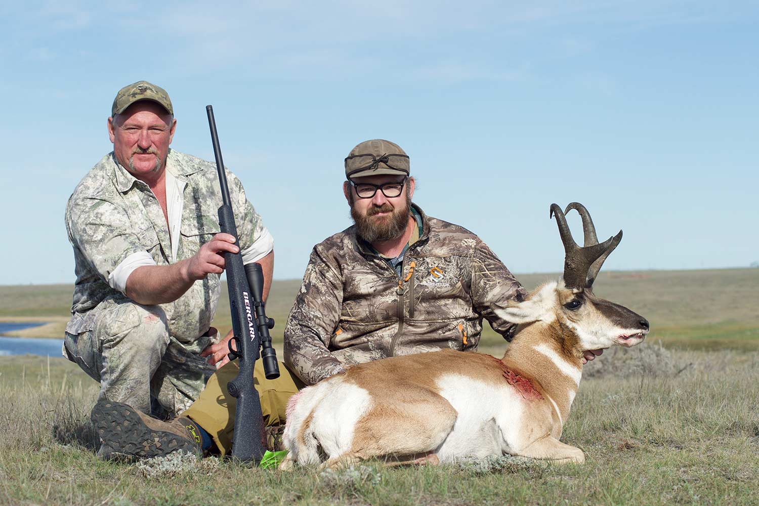 Two hunters kneel behind an antelope.