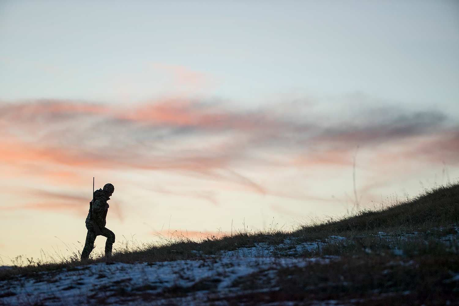 A single hunter hikes up a snowy hillside in the morning light.