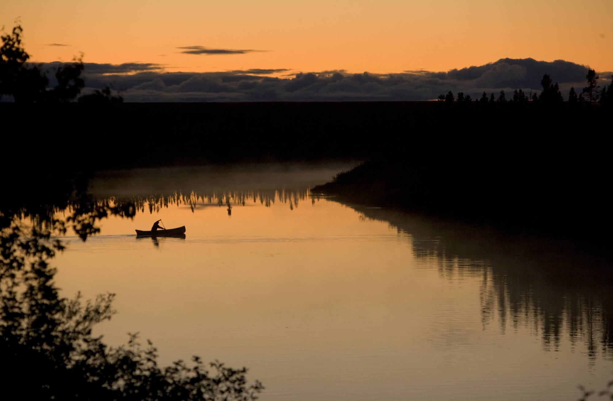 Silhouette of a paddler canoeing across a calm lake at sunrise or sunset