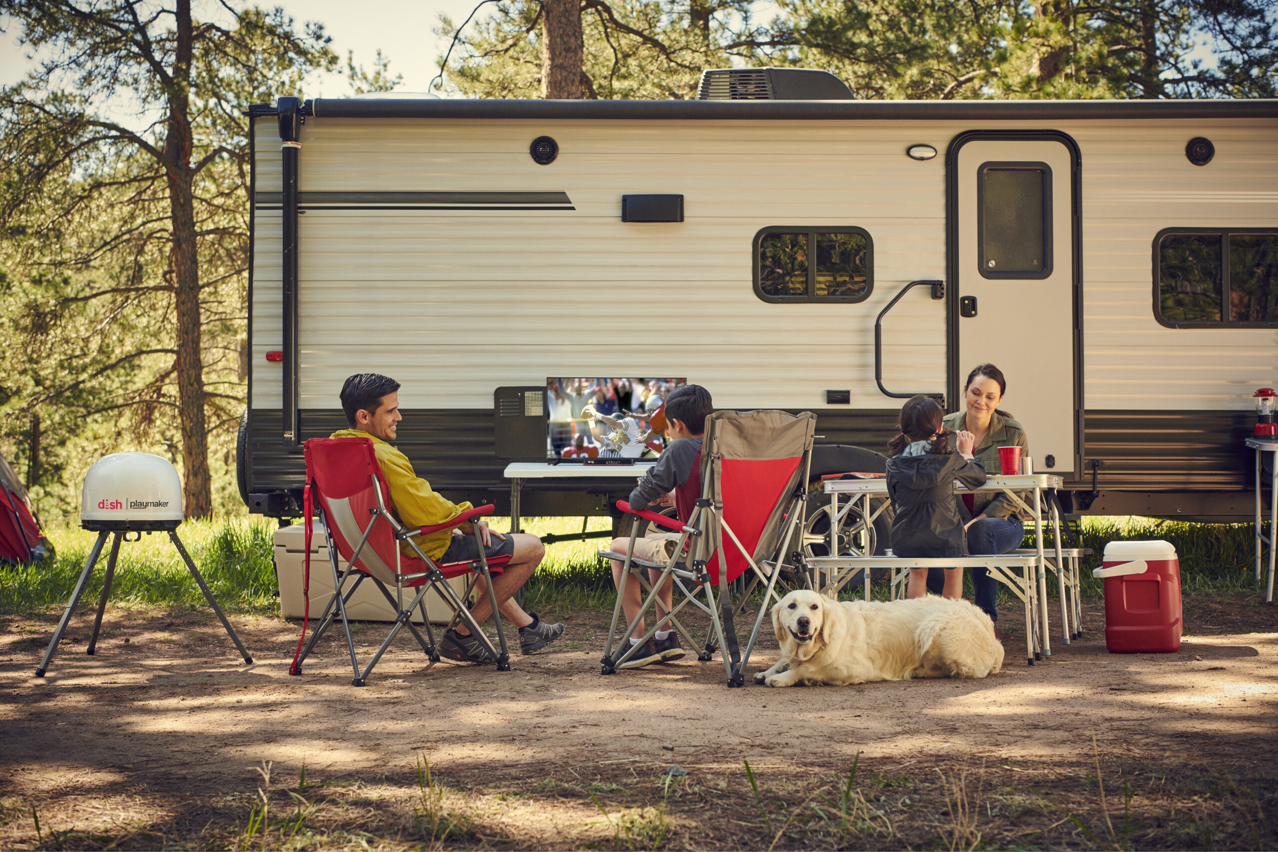 A campsite with people and dogs and a DISH Outdoors and television.