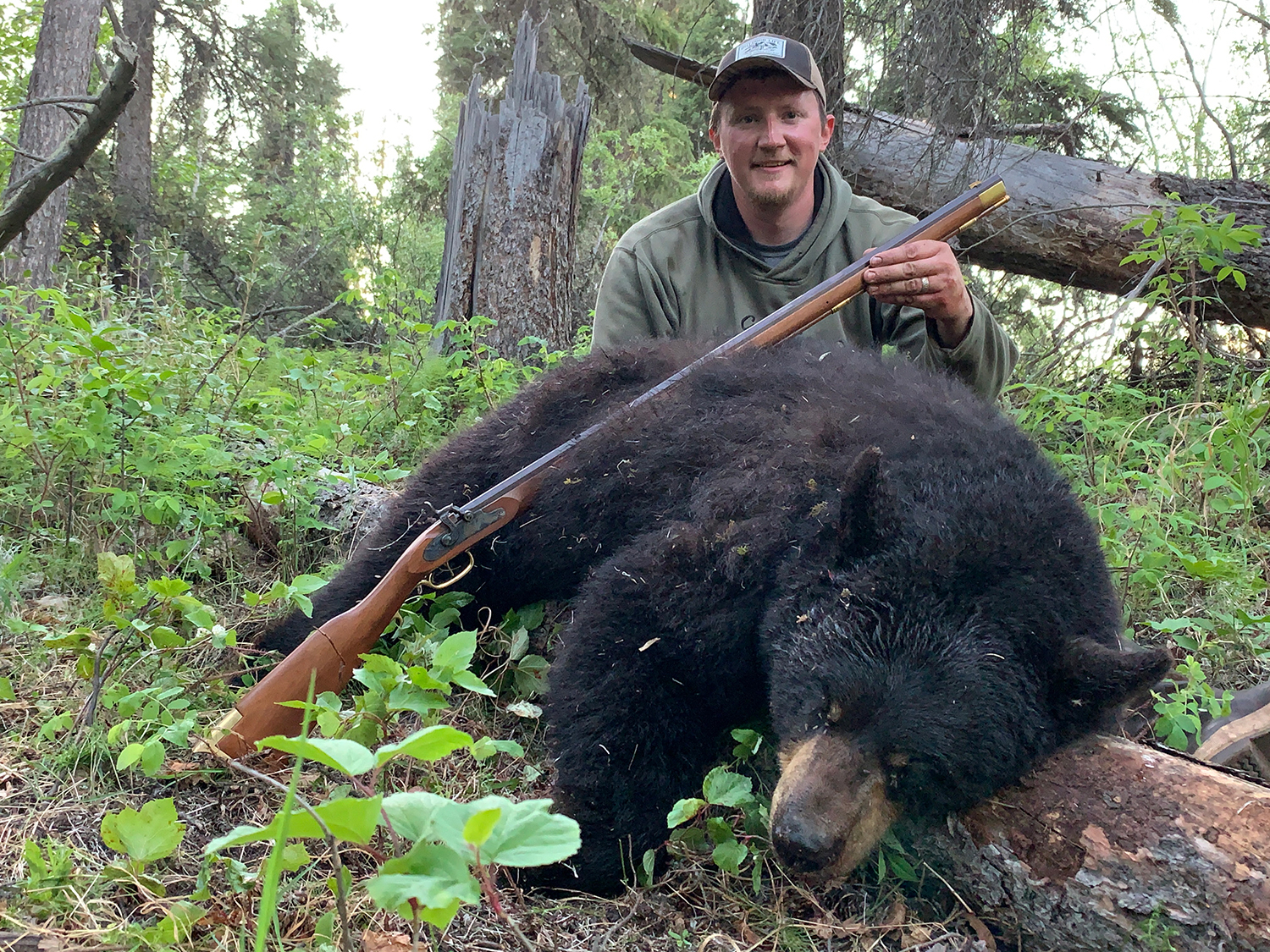 Tyler Freel kneeling behind a large spring black bear while hunting in Alaska.