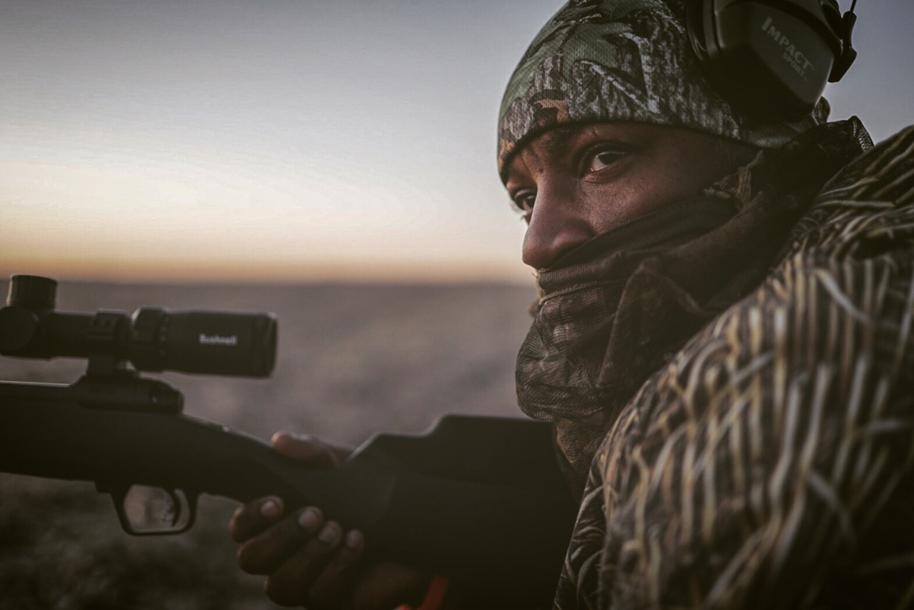 A black man in hunters camo holds a rifle.