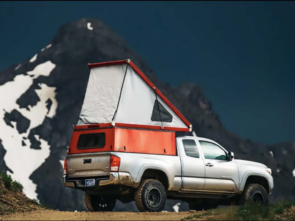 A silver truck with an orange camping tent in the truck bed.