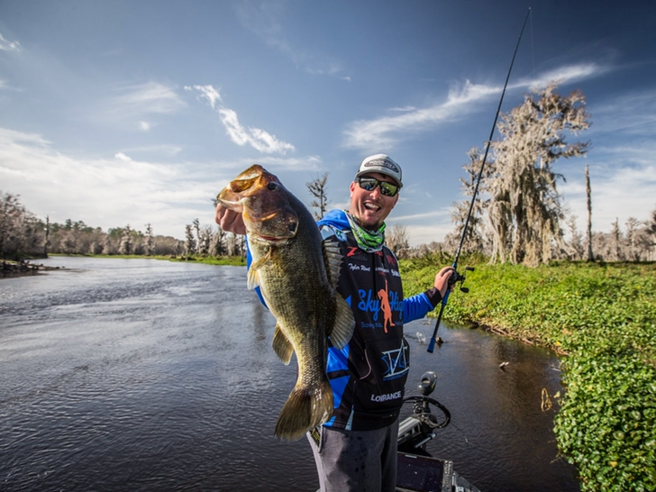 A bass fishing angler holds up a largemouth bass.