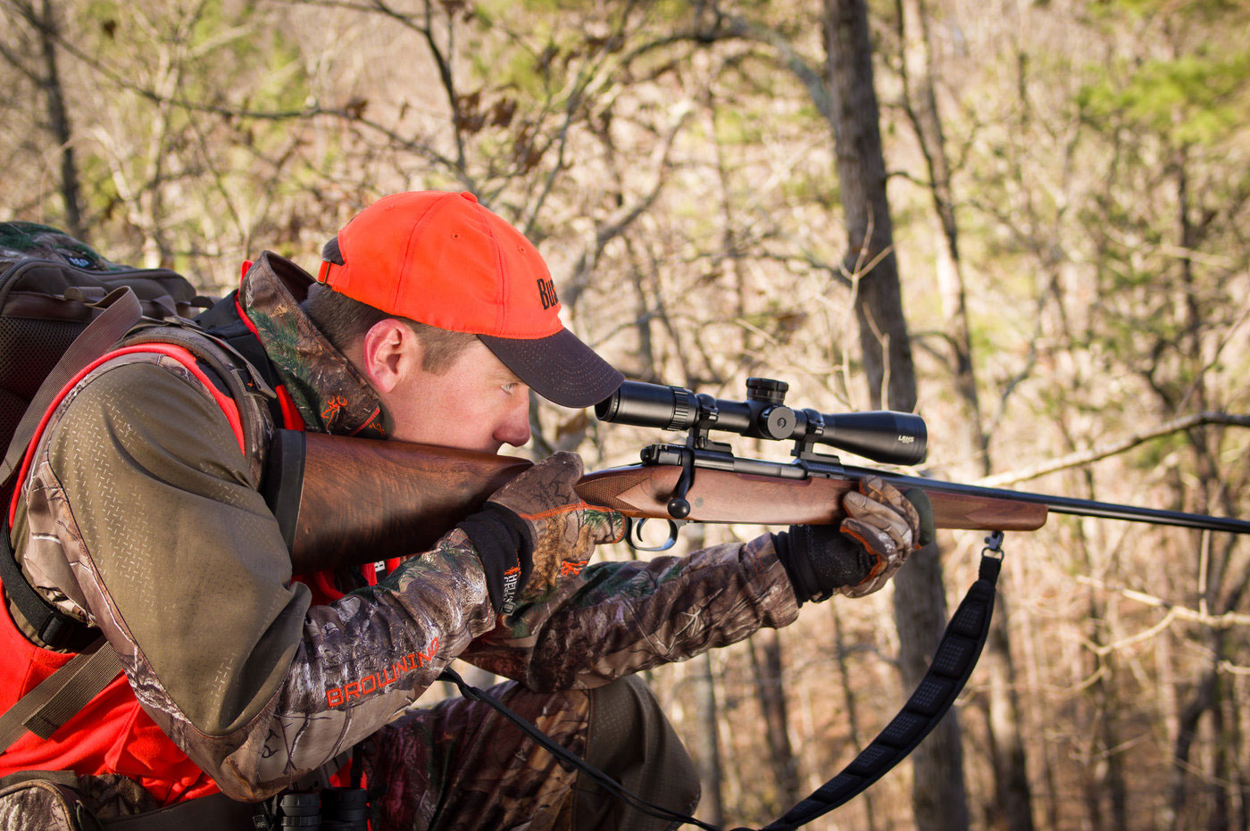 A hunter aiming a rifle in the woods.