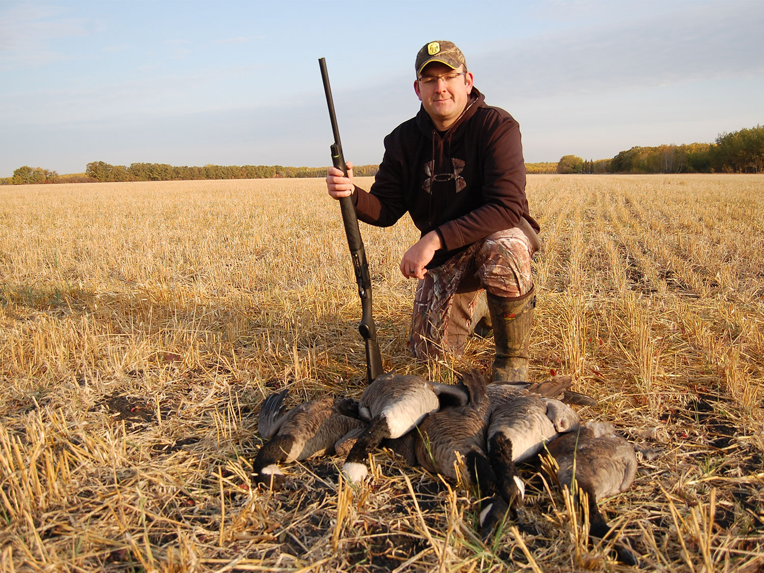 A hunter kneeling beside a limit of Canada geese.