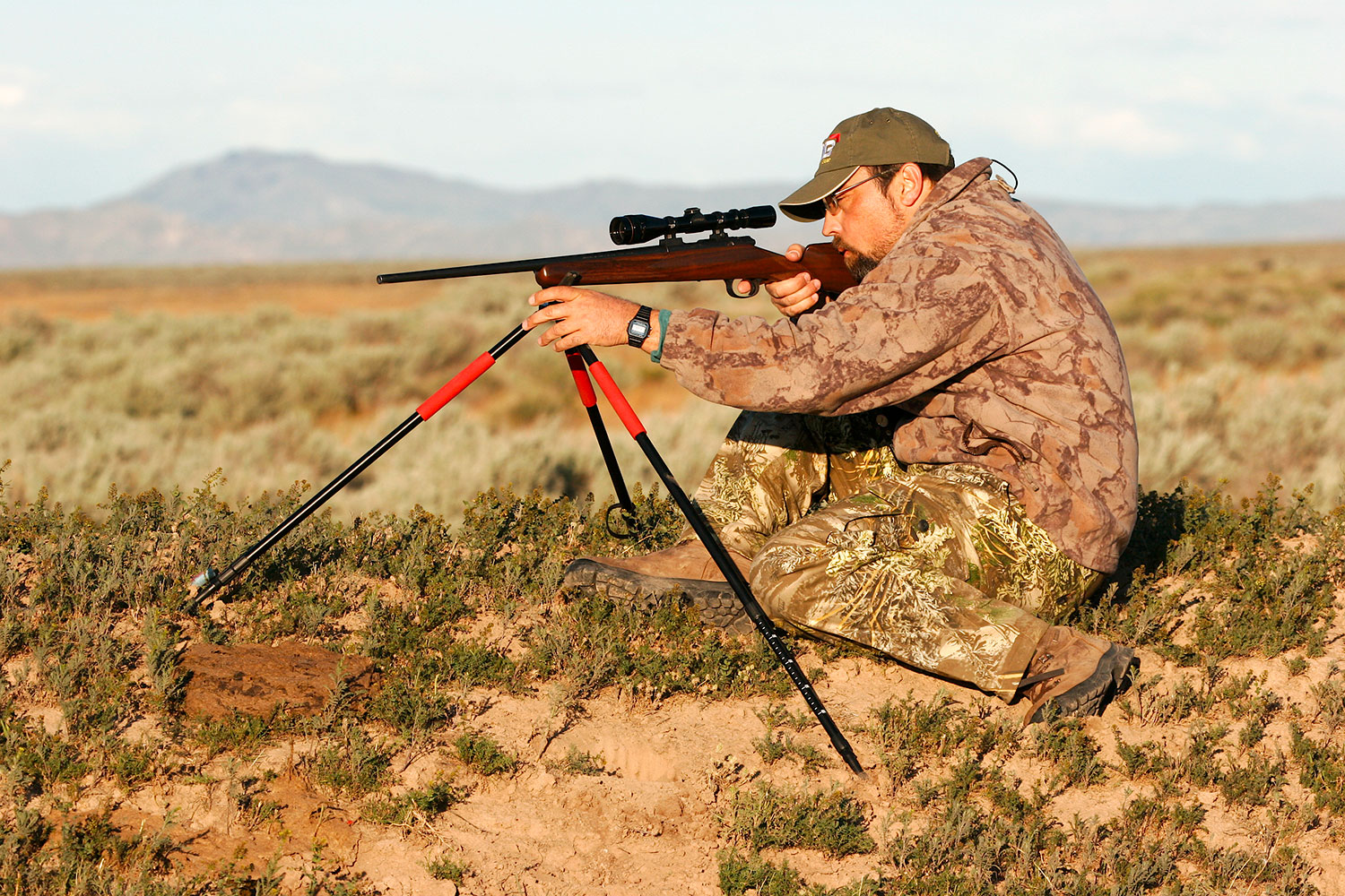 A man using a tripod to aim a rifle.