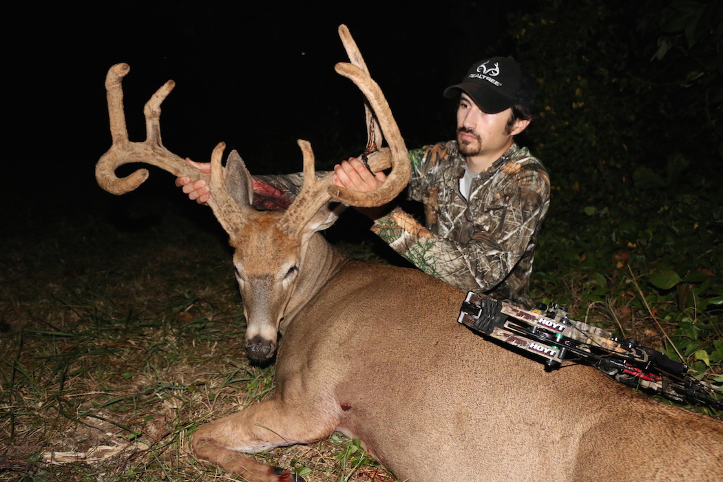 A hunter kneeling behind and holding the antlers of a large buck.