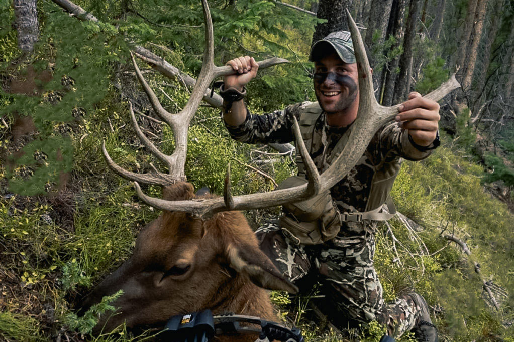 A hunter kneeling behind a giant elk.