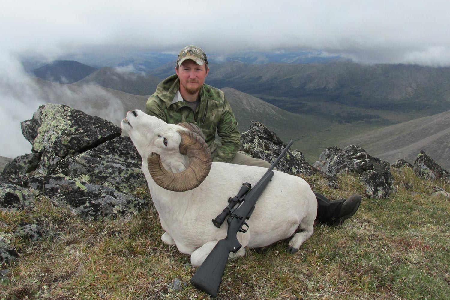Tyler Freel kneeling behind a large white mountain goat.