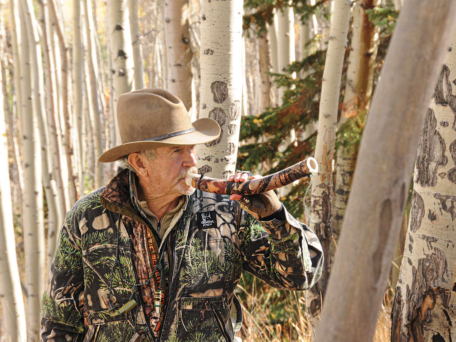 A hunter in camo and cowboy hat using a hunting call.