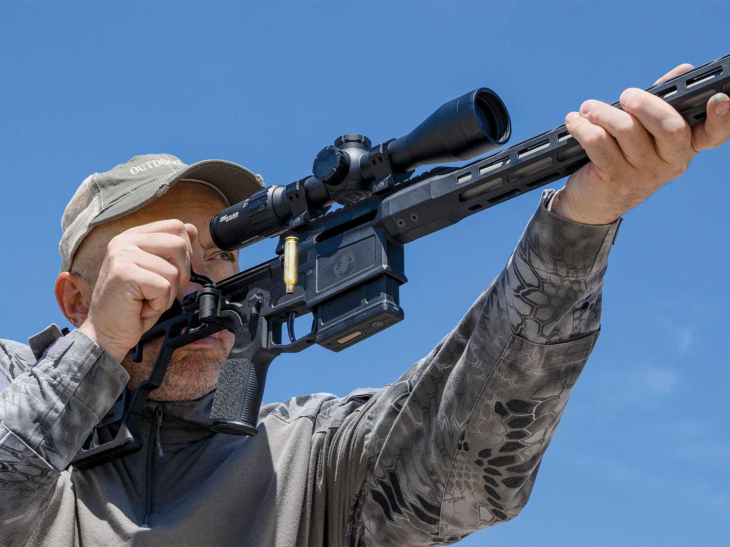 A man in a cap aims a Sig Sauer SIG Cross rifle during a gun test.