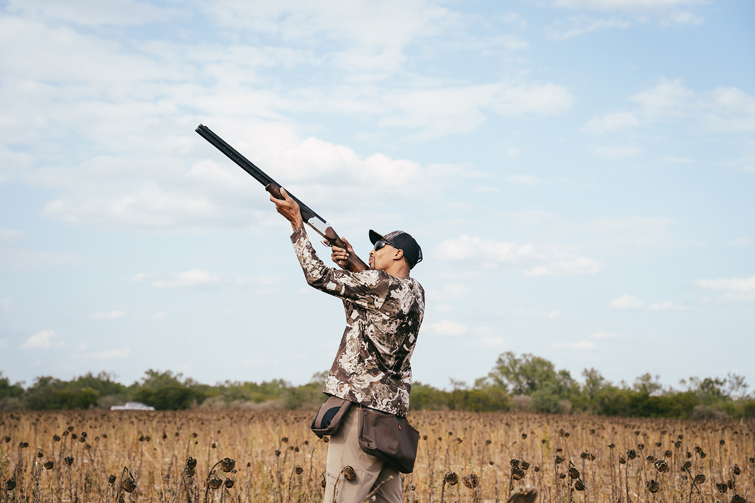 A male hunter aims a shotgun in the air.