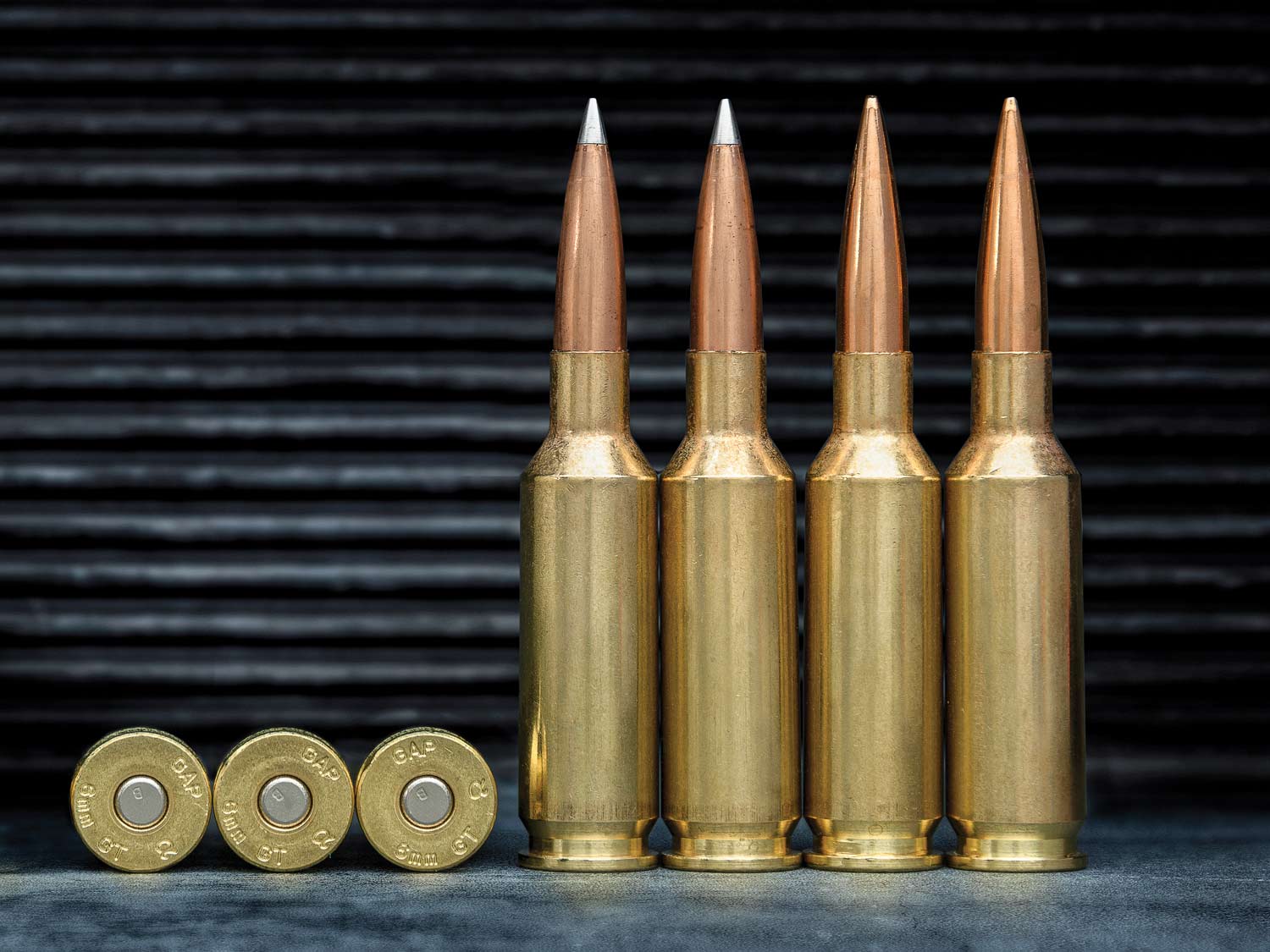 A lineup of rifle cartridges against a ridged black background.