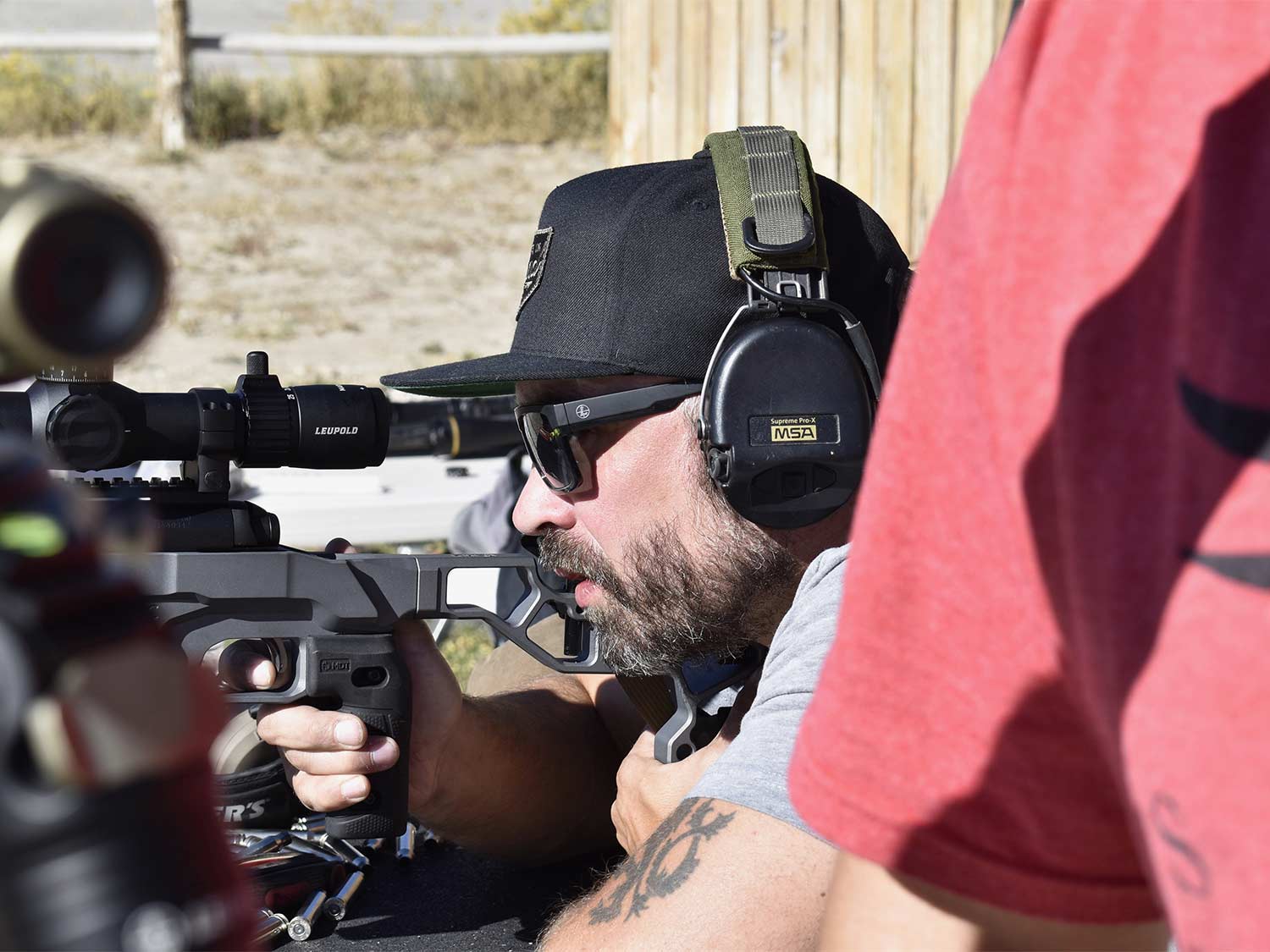 A man in glasses and hat looks through a rifle scope.