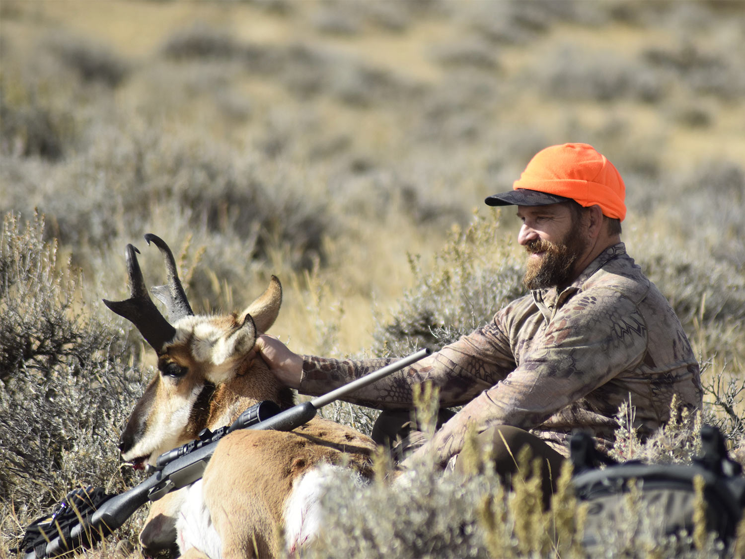 A hunter in orange sits and poses behind a dropped