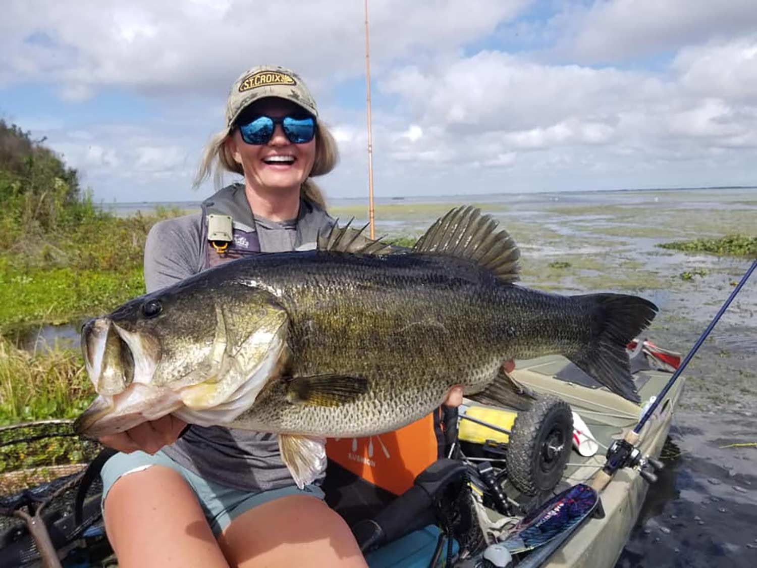 Woman angler holds up a largemouth bass while fishing from her kayak.