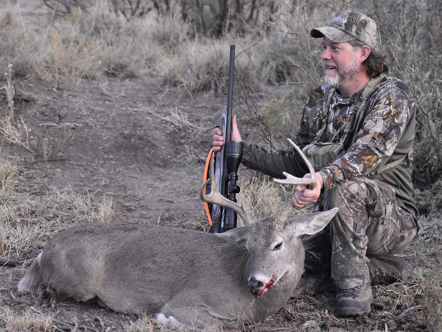 A hunter kneels next to a whitetail buck.