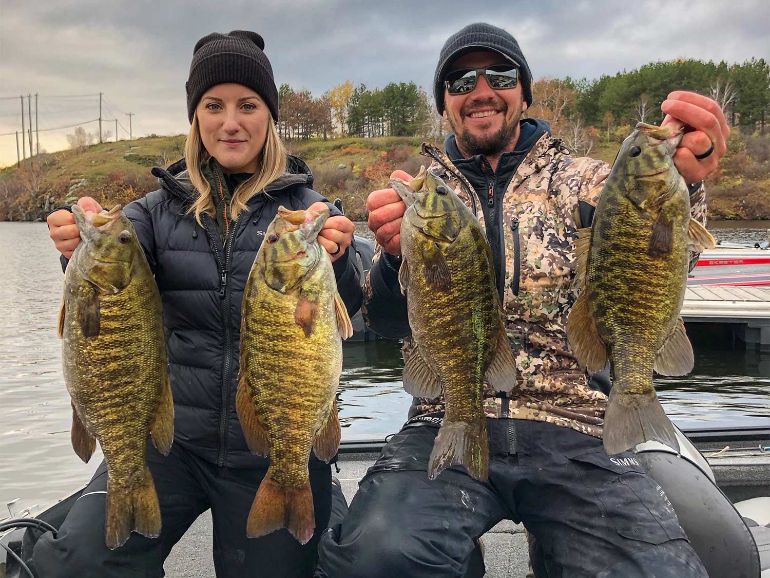 Two anglers hold up four smallmouth bass.