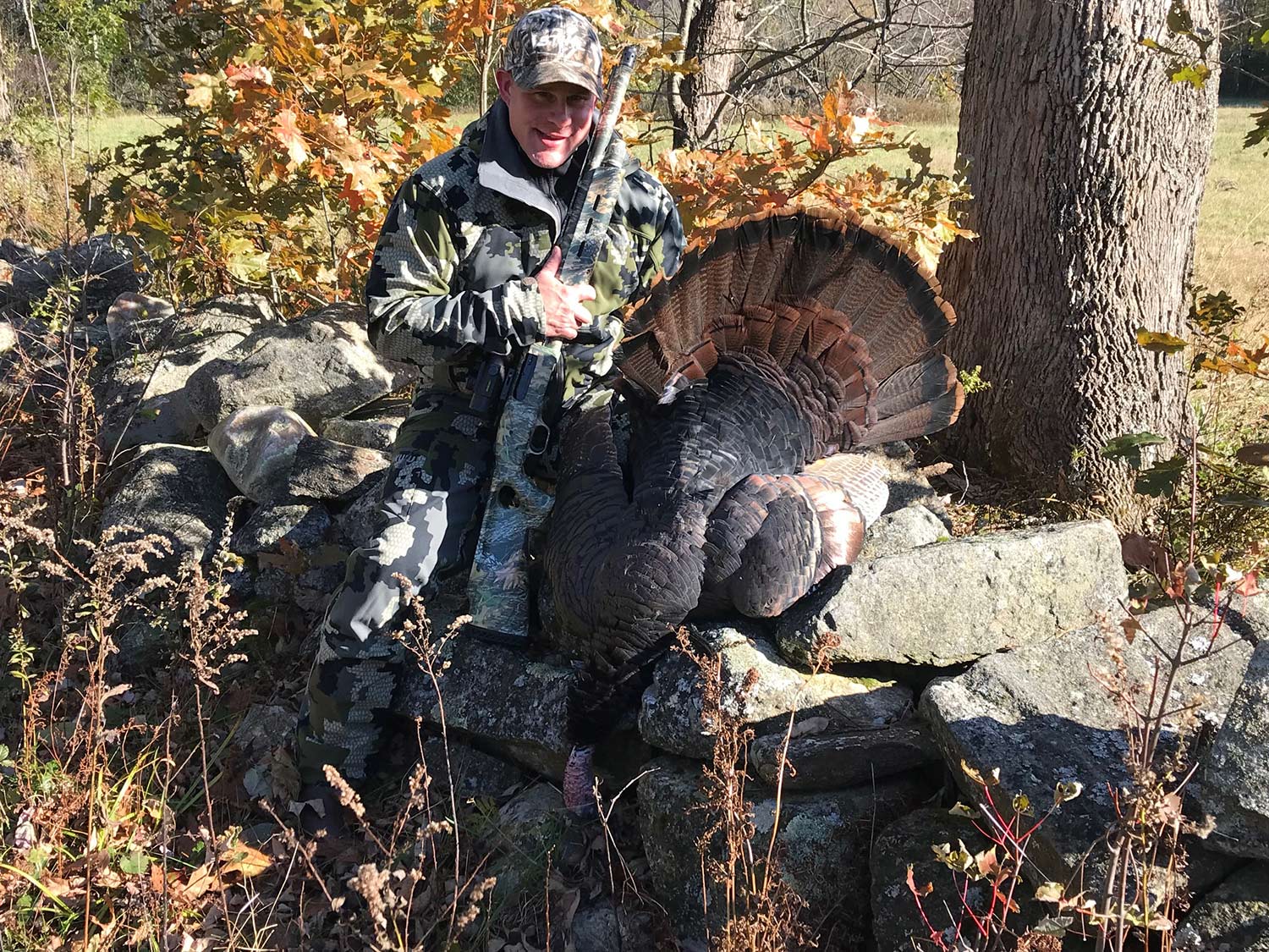 A hunter poses next to a turkey on a rock.