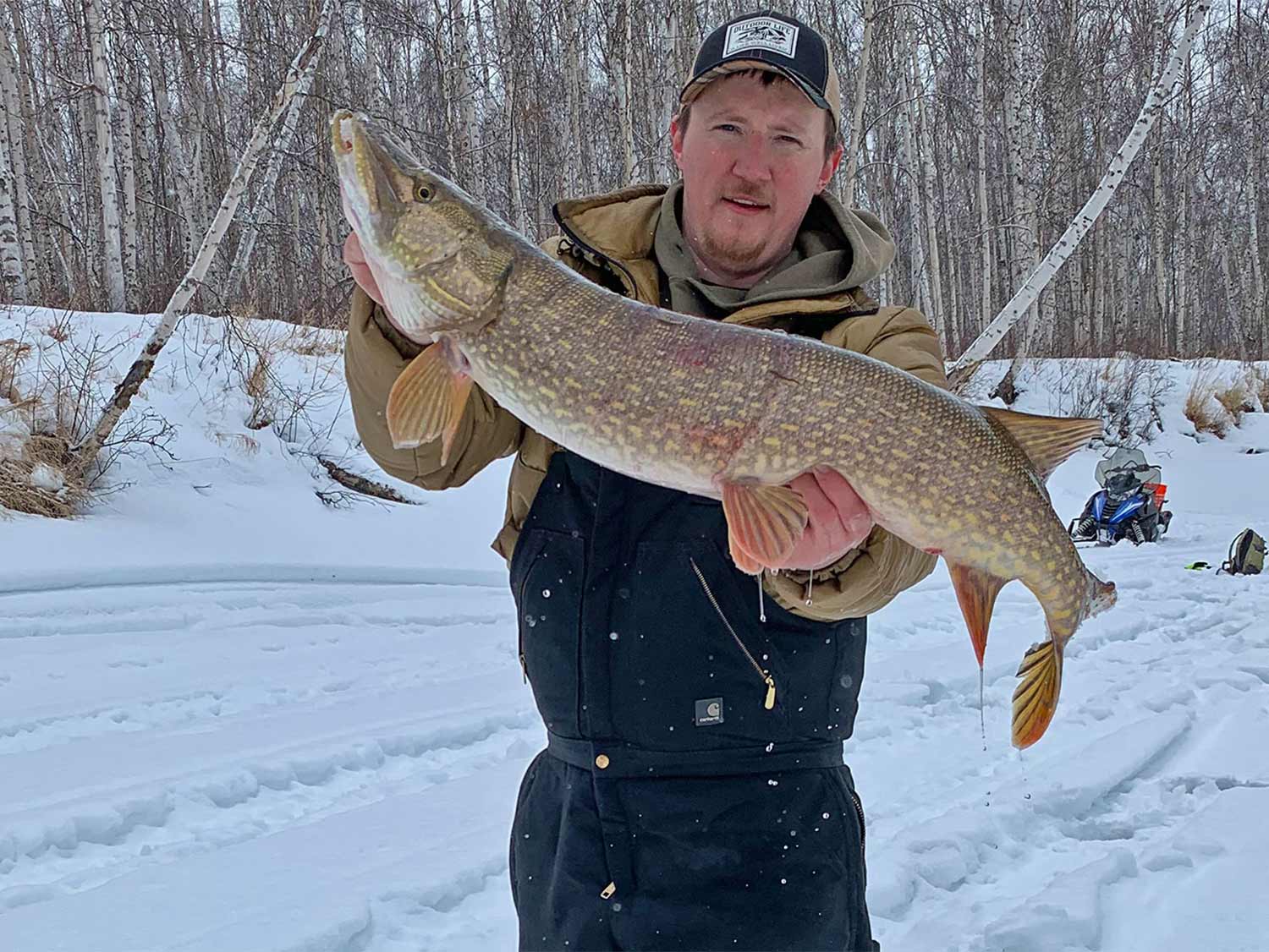 An angler holding up a large pike after ice fishing.