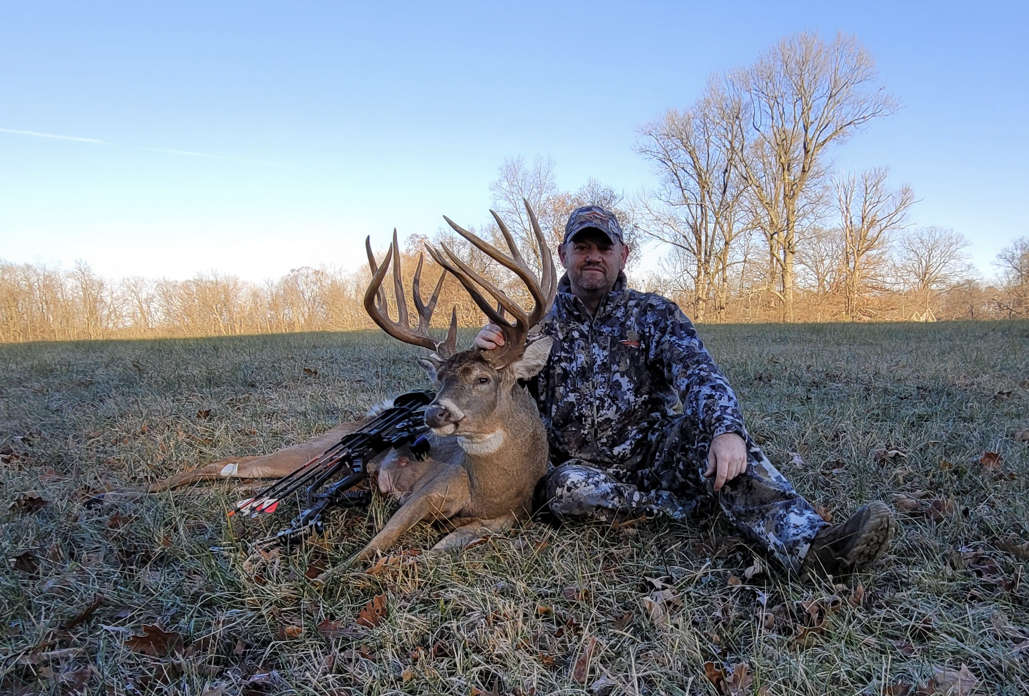 A hunter sitting beside a giant double-mainbeam whitetail buck.