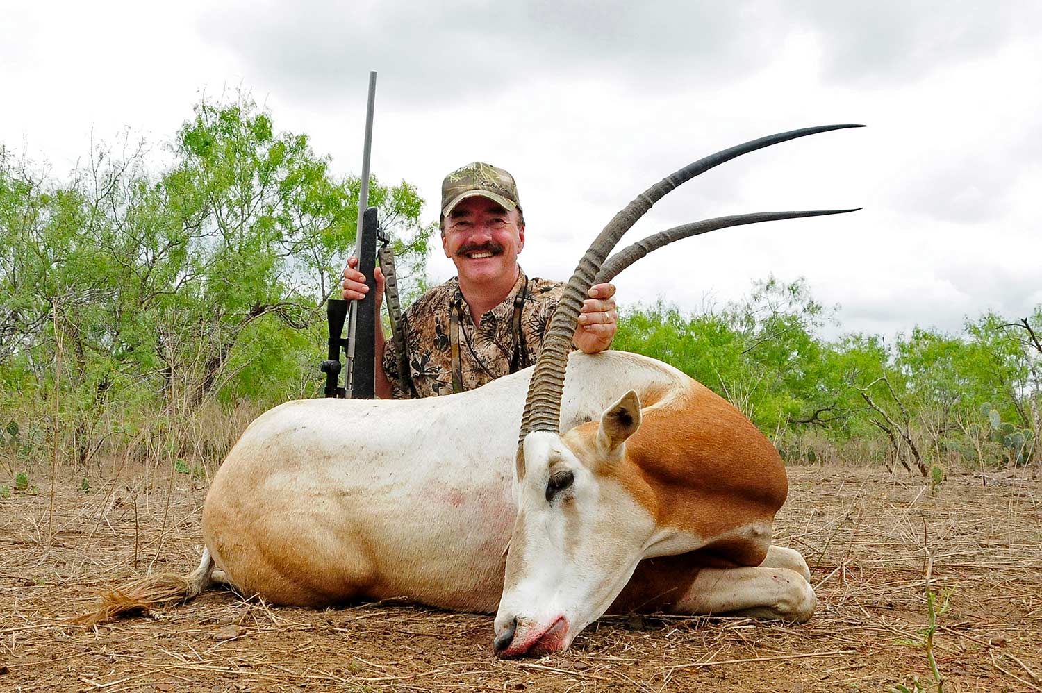 A hunter kneels behind a downed oryx in an open field.