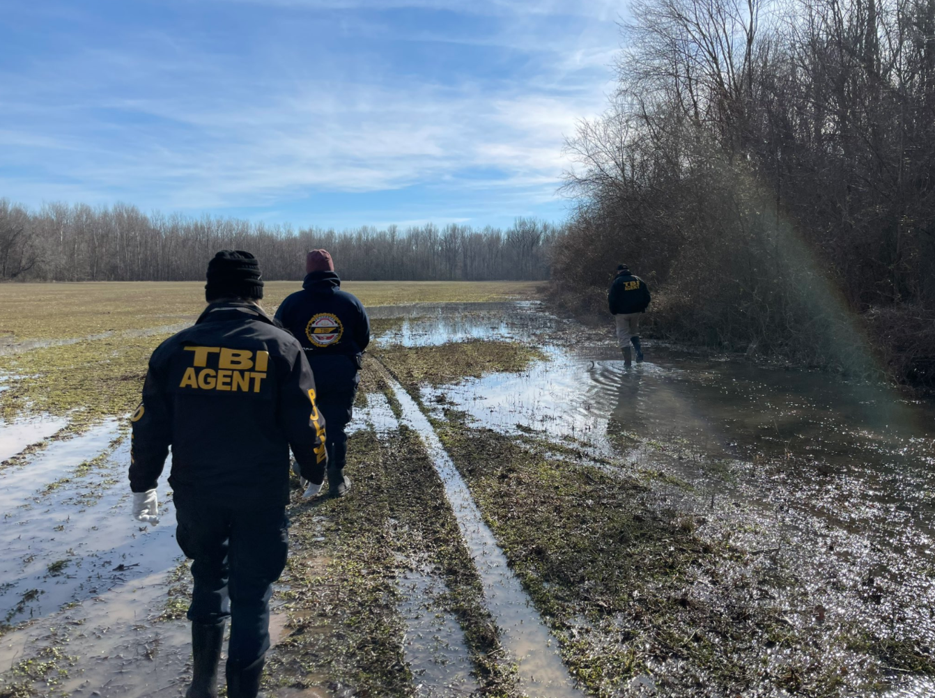 Three men in navy TBI Agent uniforms search a muddy wet field for David Vowell.