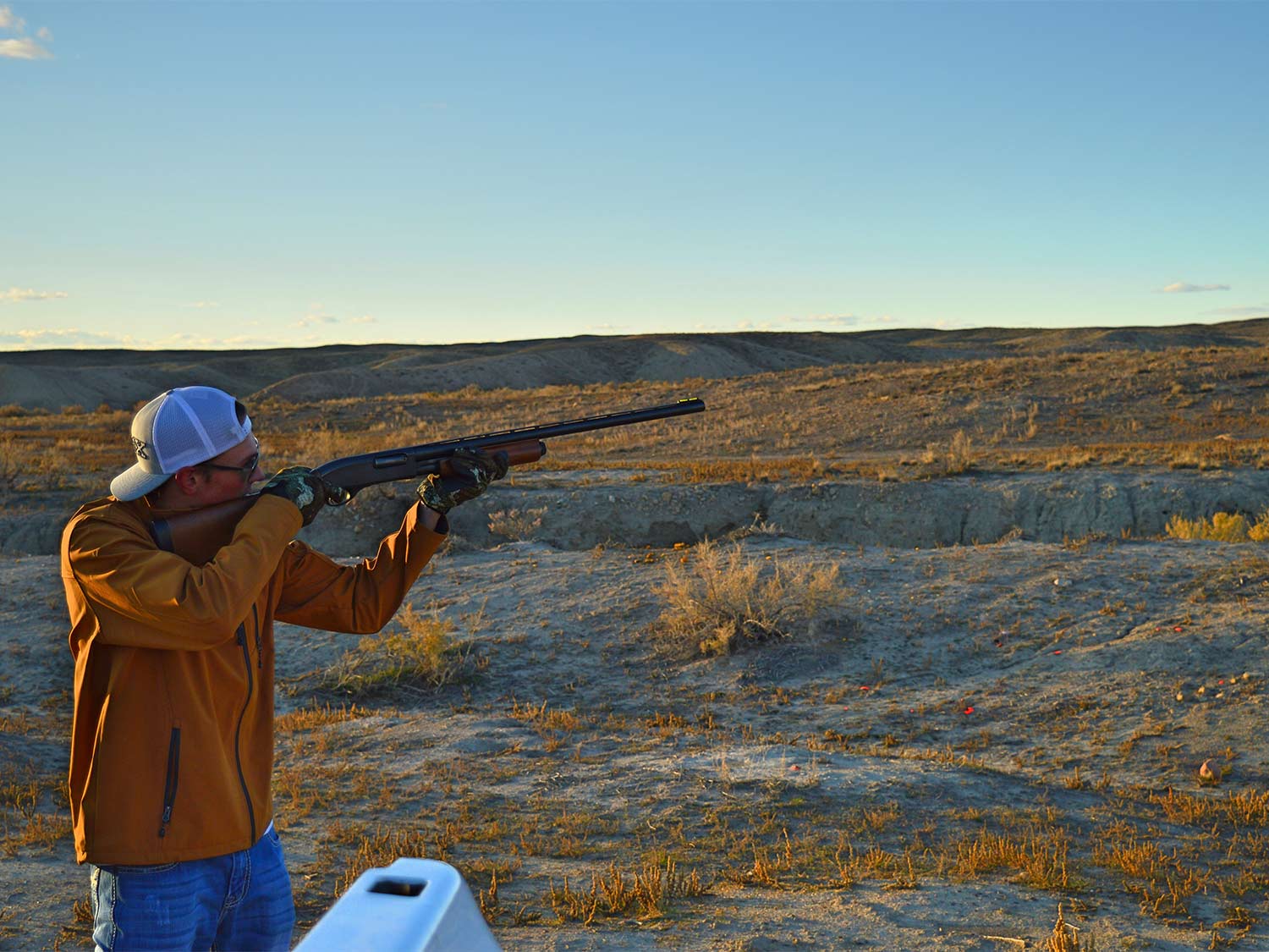 A man aims a shotgun in a large open field wearing the best shooting gloves.