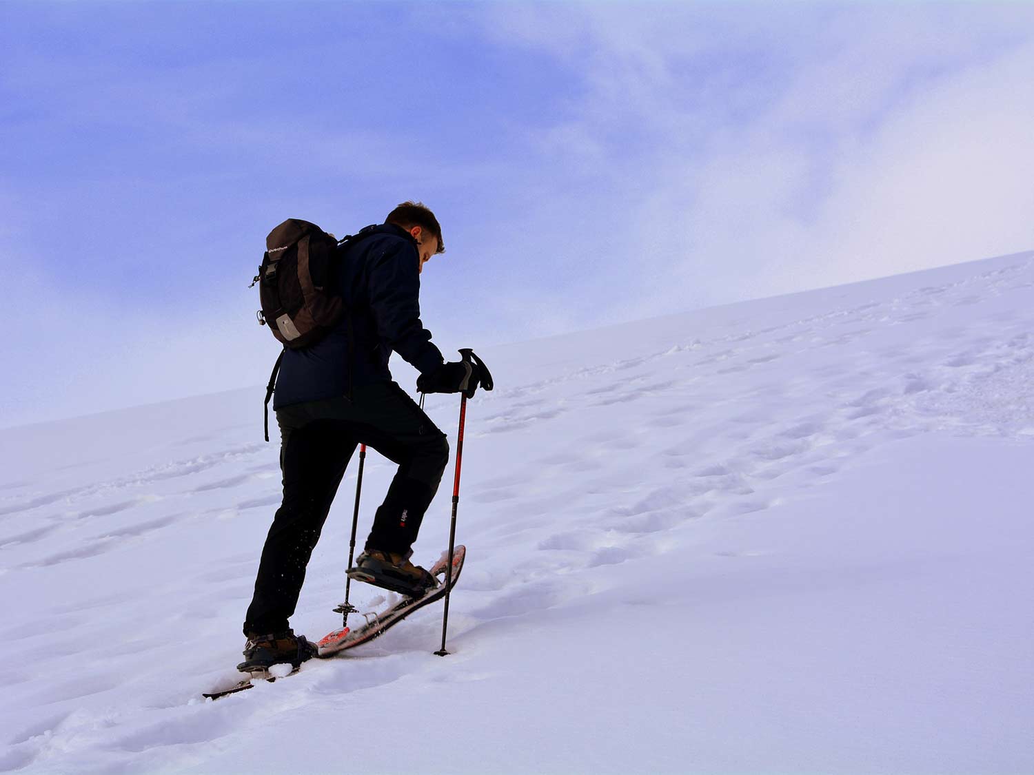 A hiker walks up a hill of snow wearing the best snowshoes.