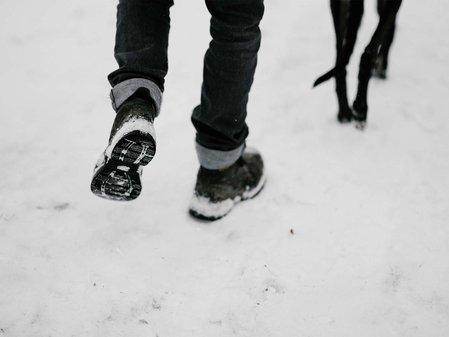 A man walks through the snow with a dog, wearing the best winter boots for men