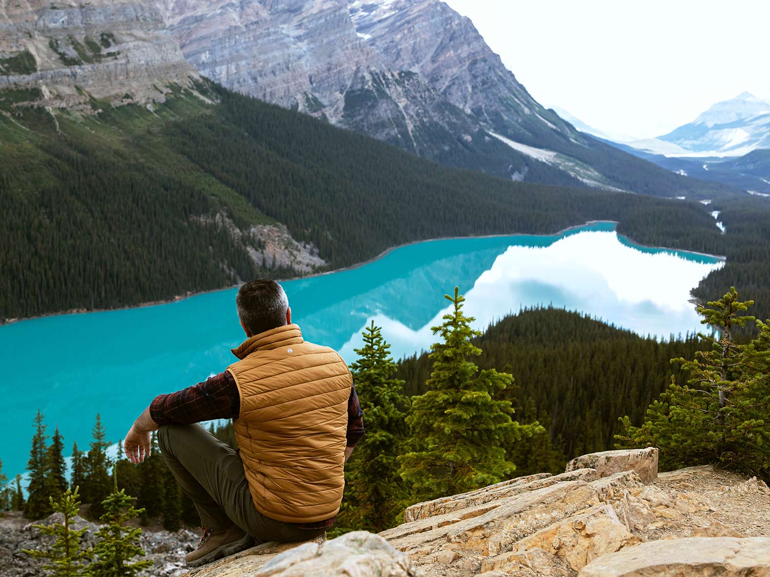 Man wearing the best heated vest, sits on a mountain side over a lake.