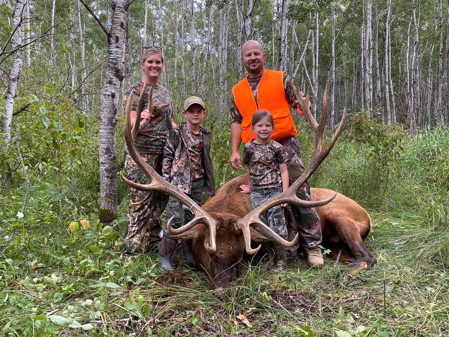 A family of four stands behind a large elk.